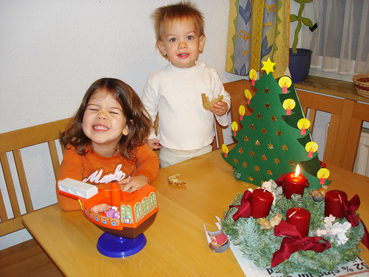 Zwei Kinder vor ihrem selbstgebastelten Adventkalender und Adventkranz mit einer brennenden Kerze