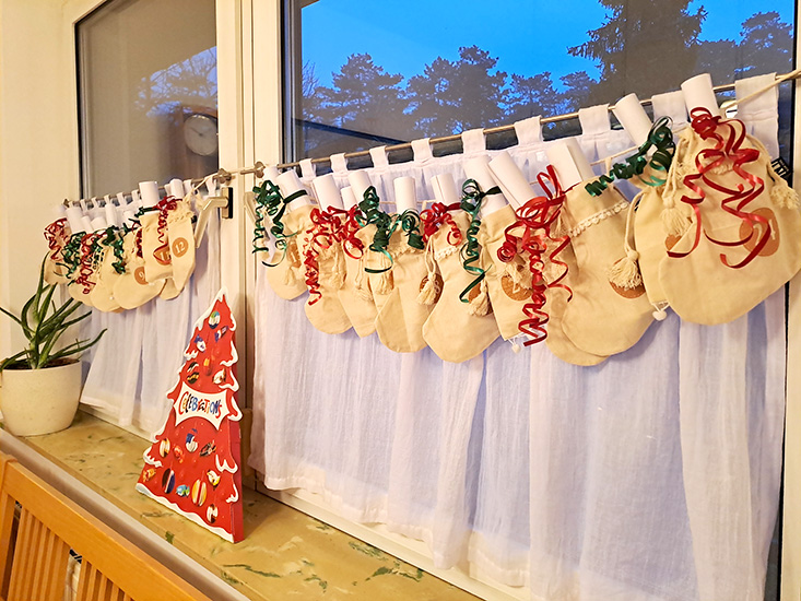 Adventkalender vor einem Fenster mit 24 Säckchen, in denen zusammengerollte Zettel stecken
