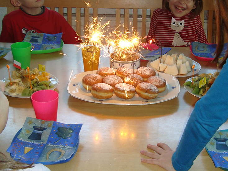 Kinder sitzen um einen Tisch, auf dem ein Teller mit Faschingskrapfen steht, auf denen 4 Wunderkerzen die Jahreszahl 2009 ergeben