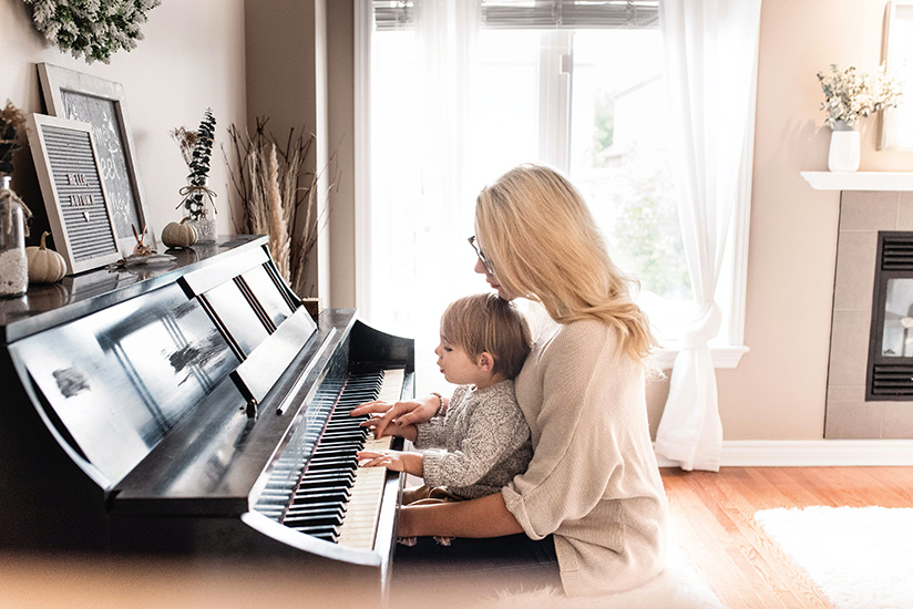 Mutter mit Kleinkind am Schoß spielen zusammen Klavier